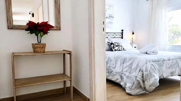 A bedroom with a bed, a bedside table with a potted plant, a mirror, and a wall-mounted light fixture.