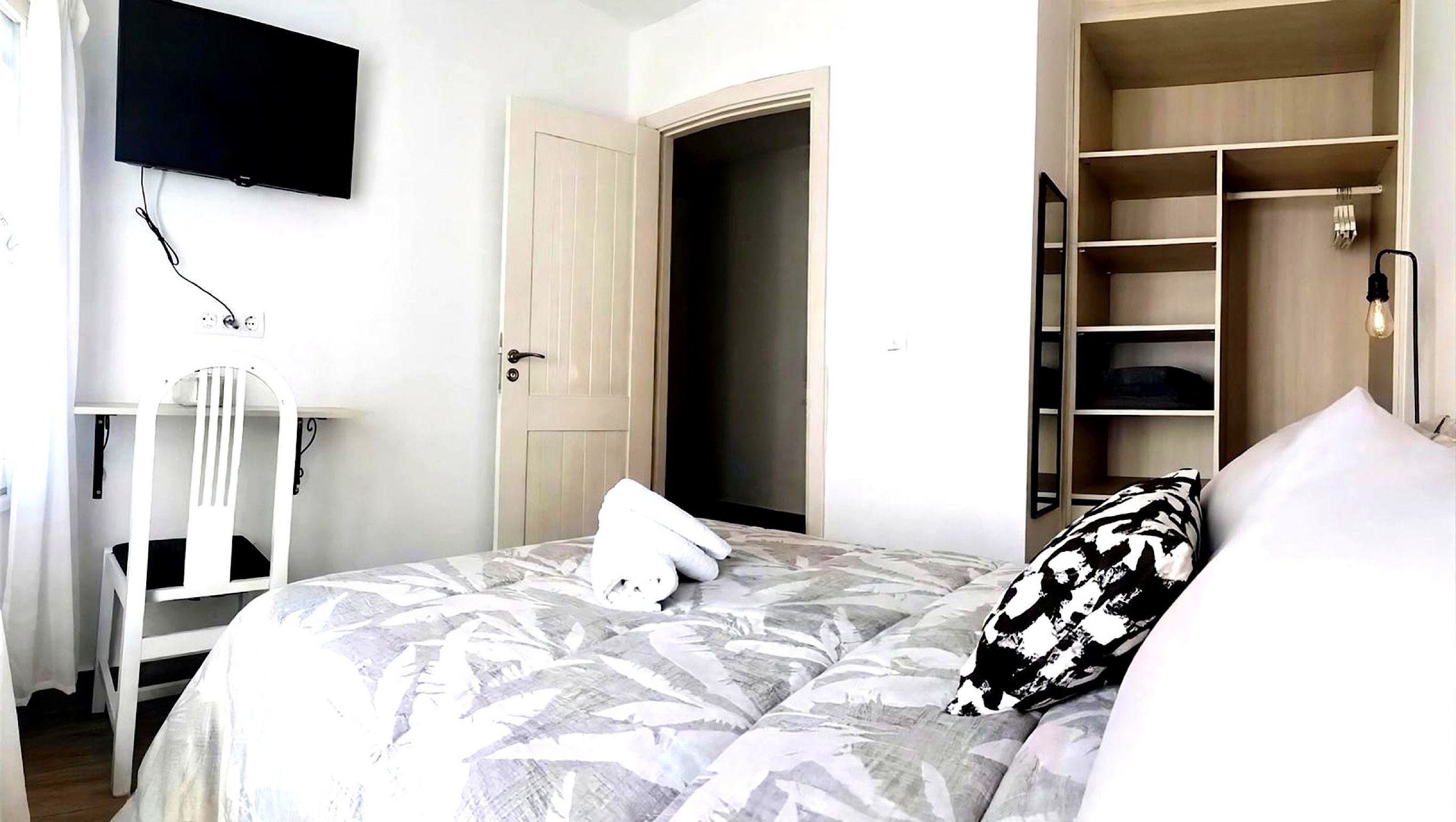Une chambre d’hôtel comprenant un lit, une armoire, un téléviseur fixé au mur et une porte donnant sur une autre pièce.