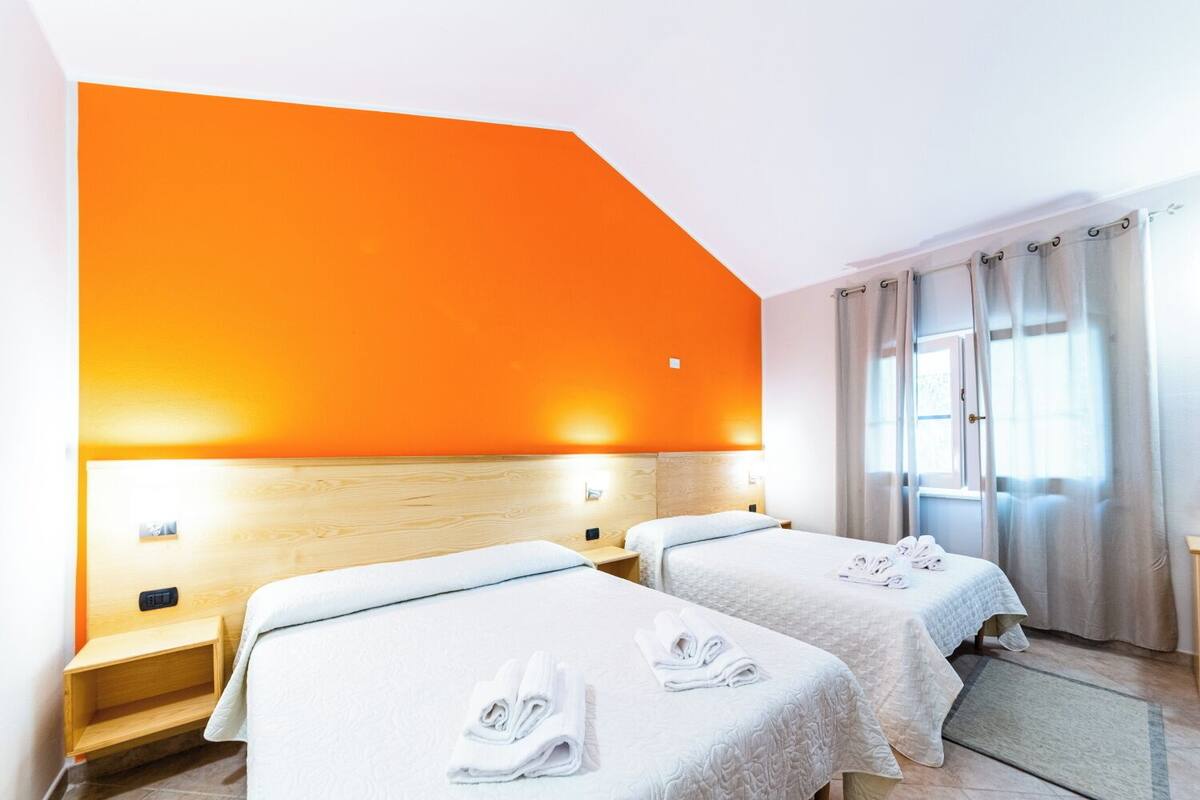 A hotel room with two beds, orange walls, and a window with curtains.