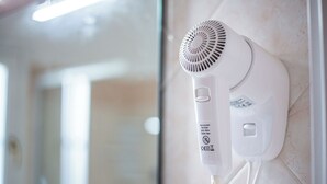 Ein an der Wand befestigter Haartrockner mit Bedienfeld, Netzkabel und Sicherheitshinweis.