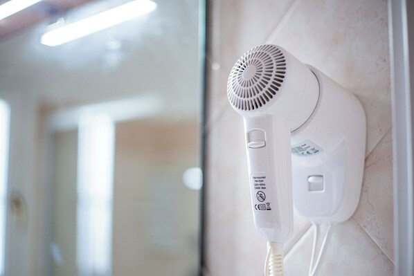 A wall-mounted hair dryer with a control panel, a power cord, and a safety warning label.