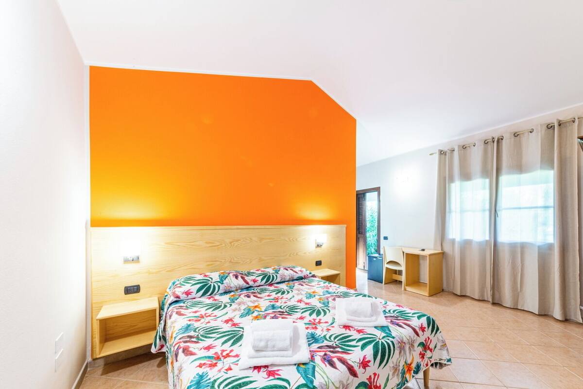 A hotel room with a bed, a desk, and a window with curtains.
