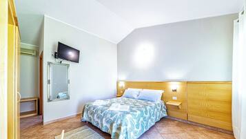 Un dormitorio con cama, televisor montado en la pared, cabecera de madera y mesita de noche con lámpara.