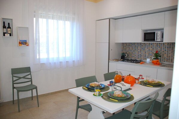 Una cocina moderna con armarios blancos, un microondas y una estufa. Hay una mesa de comedor con platos y un vaso de jugo de naranja.