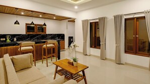 Ein modernes Wohnzimmer mit Couch, Holztisch und Küchenbereich, ausgestattet mit Holzschränken und Pendelleuchten.