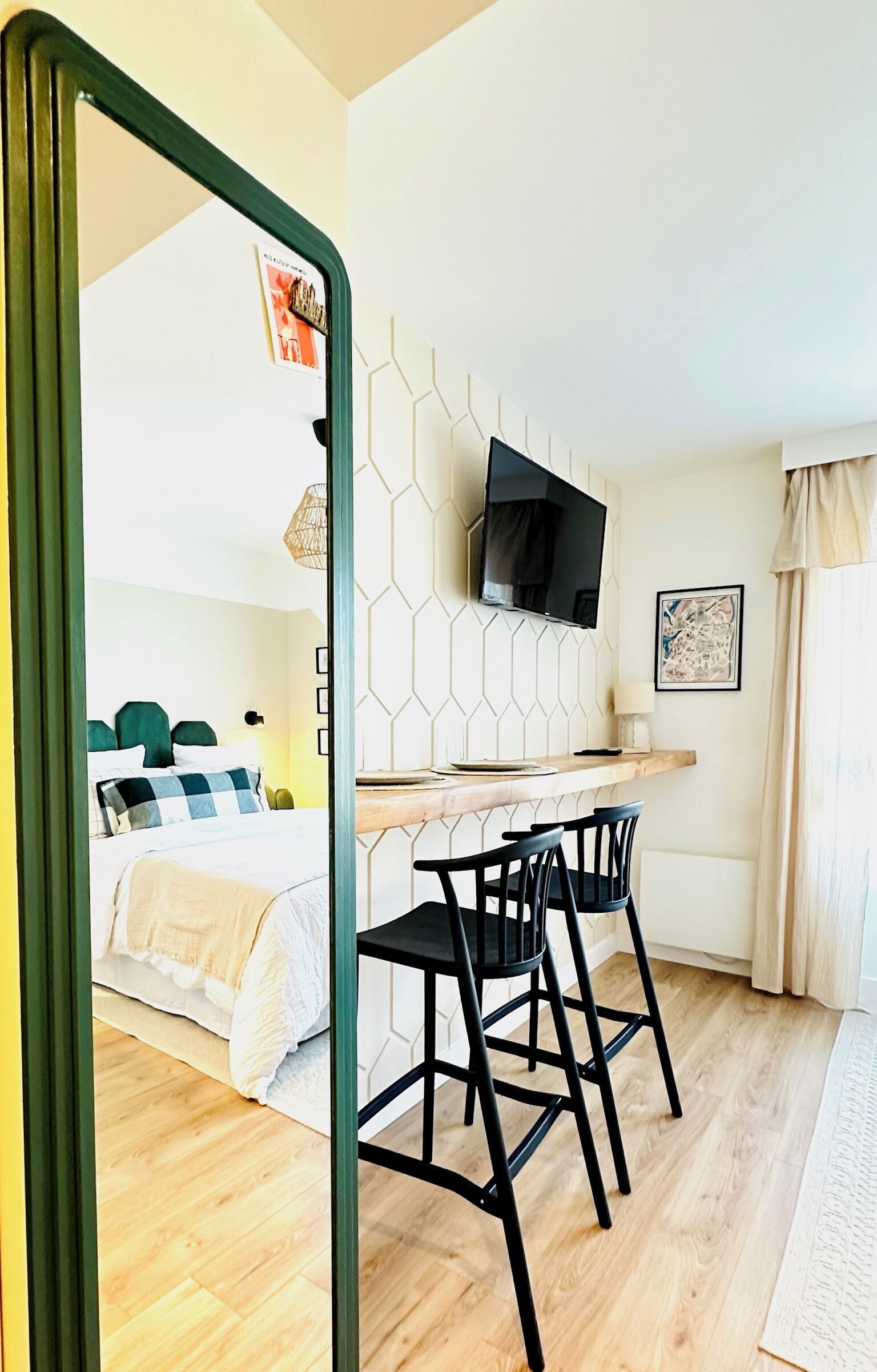 Ein kleines Zimmer mit einem Bett, einem Schreibtisch mit zwei Stühlen, einem an der Wand befestigten Flachbildfernseher und einem Fenster mit Vorhängen.