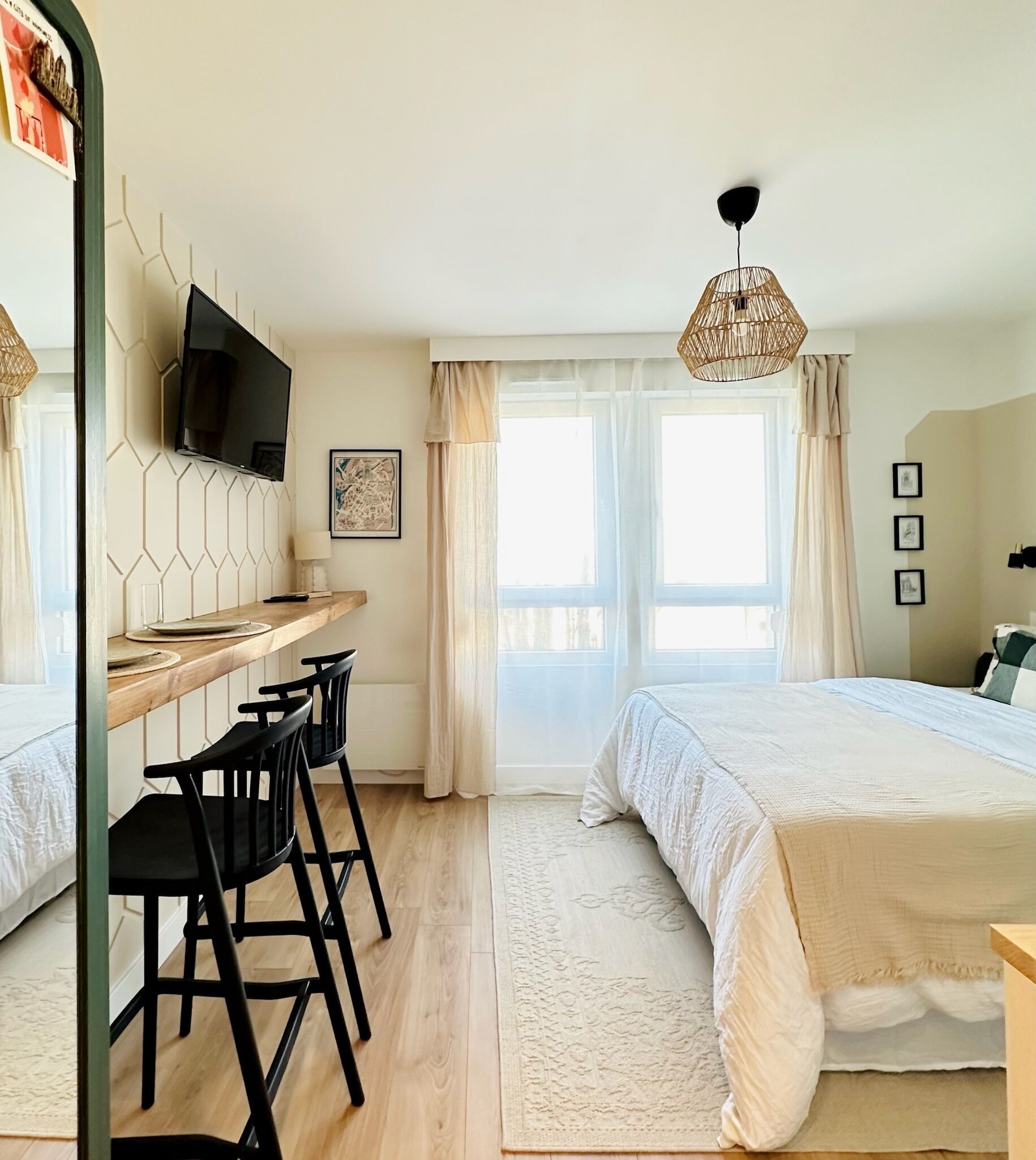 Un dormitorio con una cama, un escritorio con sillas, un televisor y una ventana con cortinas.