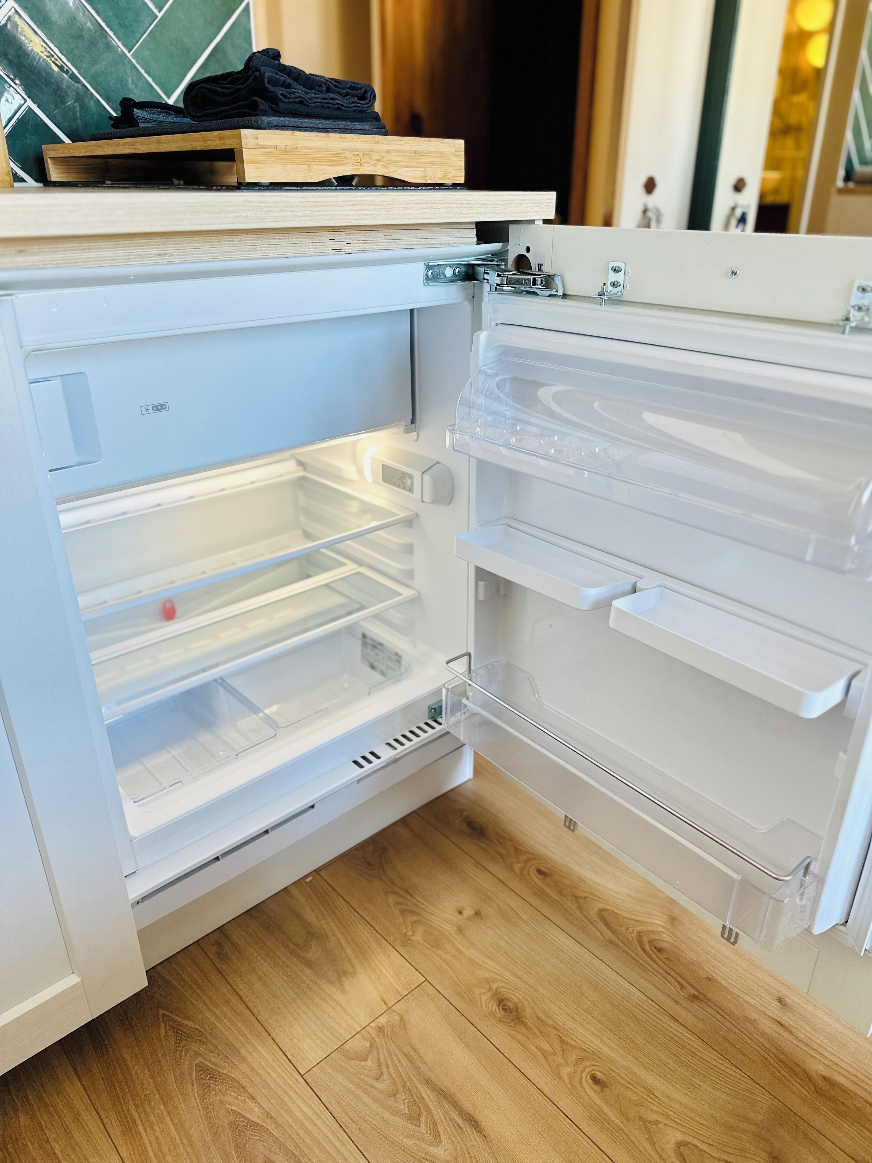 An open refrigerator with clear shelves and a wooden shelf on top.