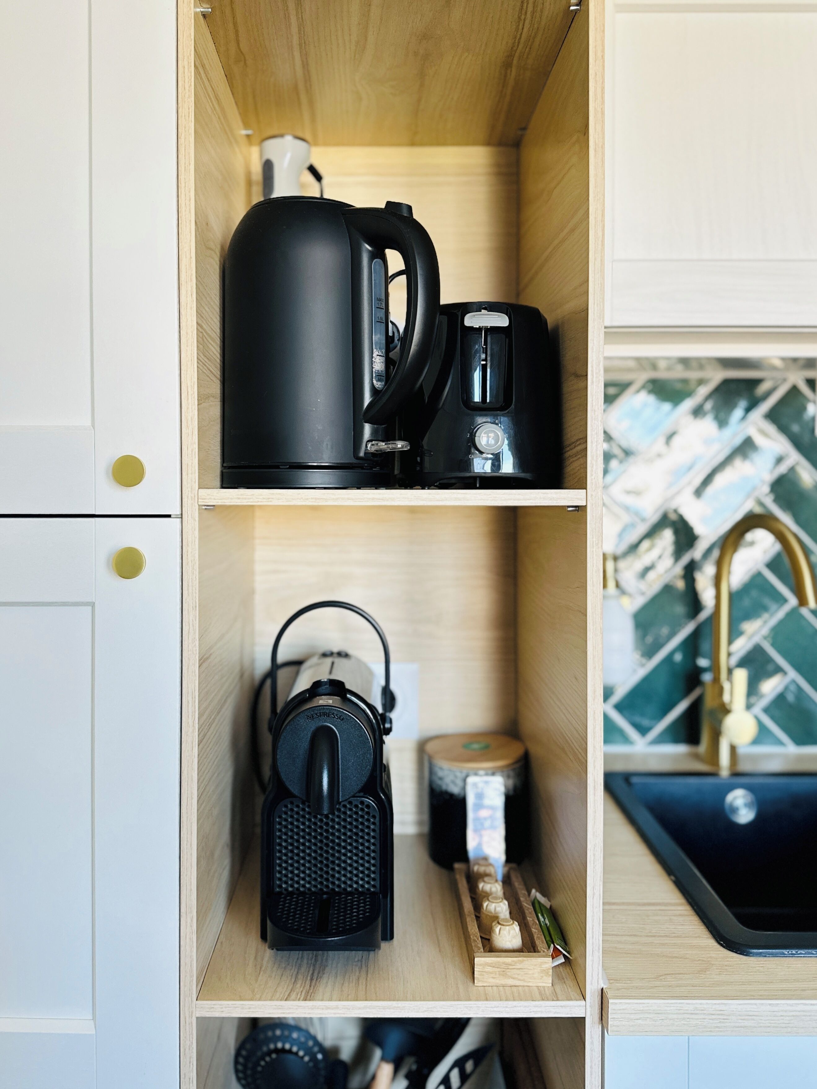 Une cuisine équipée d’une machine à café, d’une bouilloire et d’une machine à expresso, le tout placé sur des étagères.