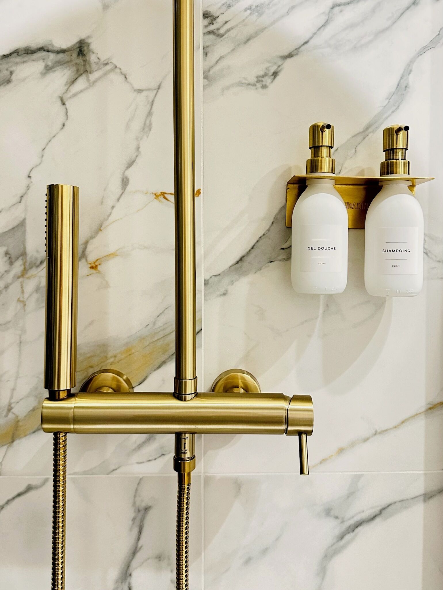 Eine goldfarbene Duschbrause vor einer Wand aus Marmor.