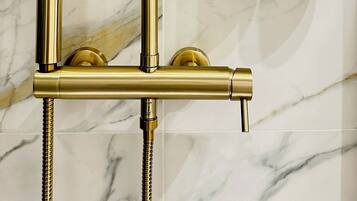 Eine goldfarbene Duschbrause vor einer Wand aus Marmor.