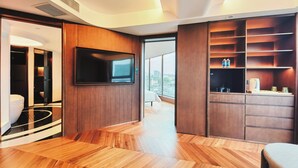 Een moderne hotelkamer met een grote televisie, houten vloeren en uitzicht op de stad.