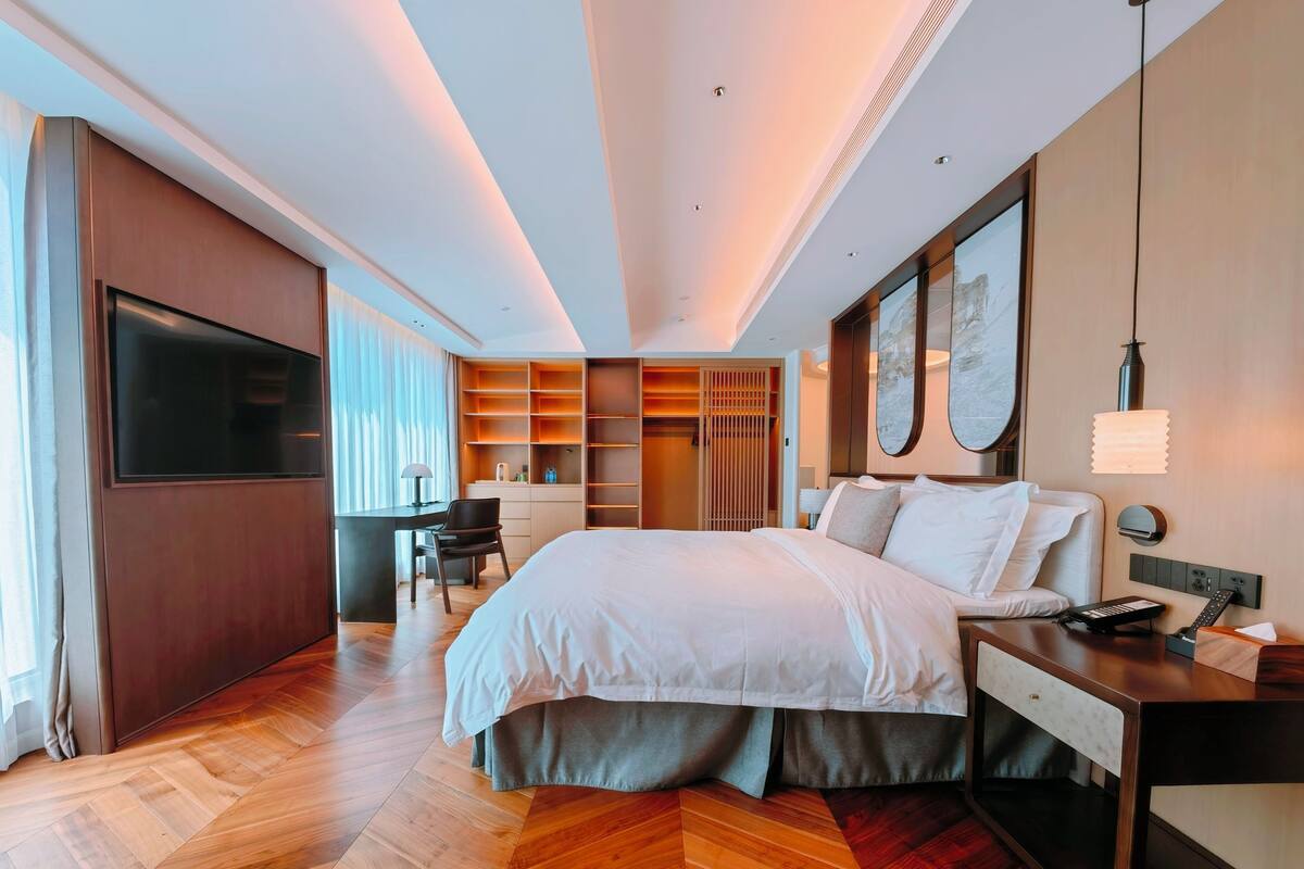 A modern hotel room with a large bed, a desk, a wardrobe, and a seating area.