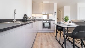 Una cocina moderna con una isla central, horno empotrado y comedor con mesa y sillas.