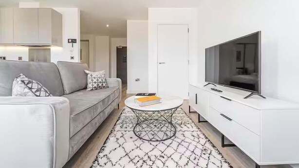 Una sala de estar moderna con un sofá gris, una mesa de centro redonda y un televisor de pantalla plana sobre un mueble blanco.