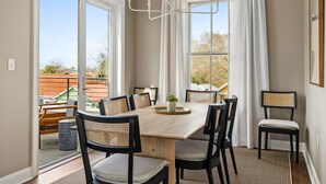 A dining area with a wooden table, six chairs, a chandelier, and large windows with curtains. - Rooftop Patio and close to King Street (Charleston)