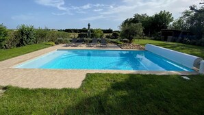 Une piscine rectangulaire, bordée d’une terrasse carrelée et entourée de pelouse et d’arbres.