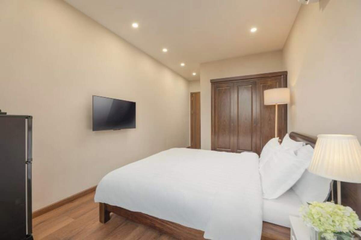 Ein Hotelzimmer mit einem Bett, einem Fernseher, einem Holzschrank und einem Nachttisch mit Lampe und Blumen.