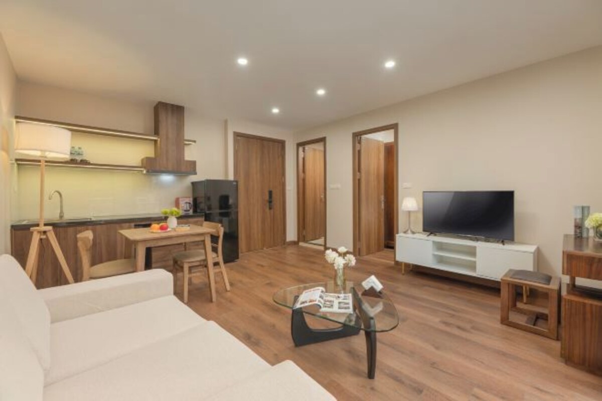 Ein modernes Wohnzimmer mit einer Couch, einem Glastisch, einem Fernseher und einer Küchenzeile mit Holzschränken und einem Esstisch.