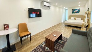 Habitación de hotel con una cama, un televisor mostrando 'NETFLIX', una silla, una mesita y un sofá.