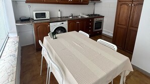 A compact kitchen with wooden cabinets, a microwave, a washing machine, and a dining table with chairs. - Casa Maia, (Arcozelo)