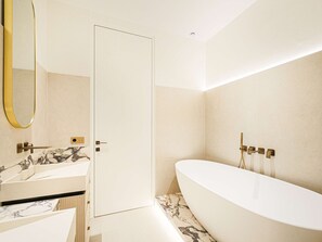 A modern bathroom with a freestanding bathtub, two sinks with marble countertops, and a large mirror.