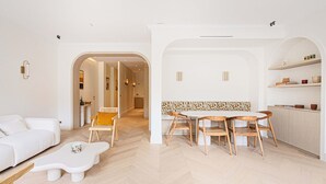 Een moderne woonkamer met een witte bank, een bijzondere salontafel, en een eethoek met houten stoelen en een witte tafel.