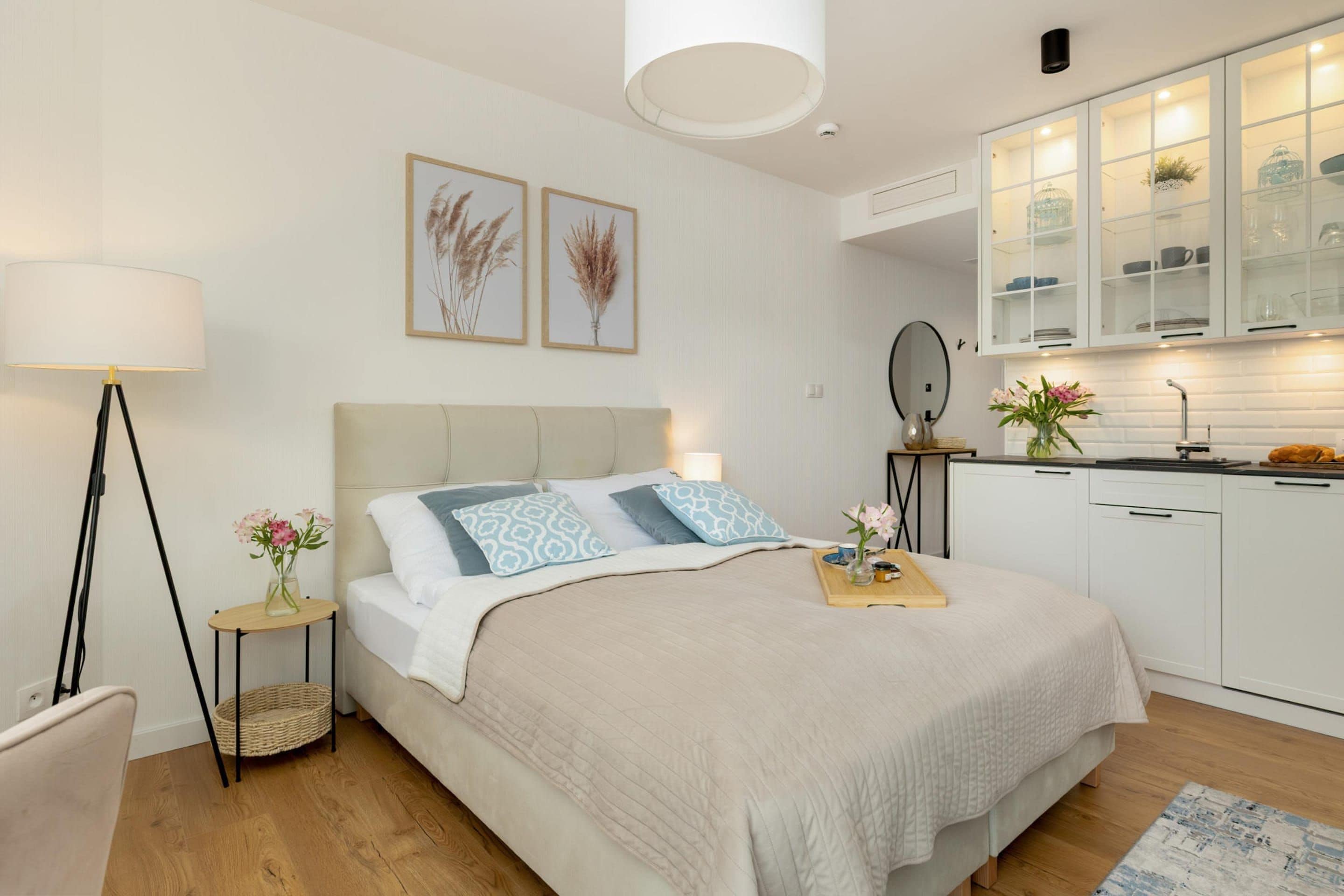 Un dormitorio con cama, mesitas de noche, lámpara y una zona de cocina con armarios y un lavabo.