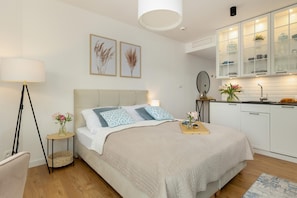 A bedroom with a bed, bedside tables, a lamp, and a kitchen area with cabinets and a sink. - Holiday Studio With Access to Pool and Sauna (Rewal)