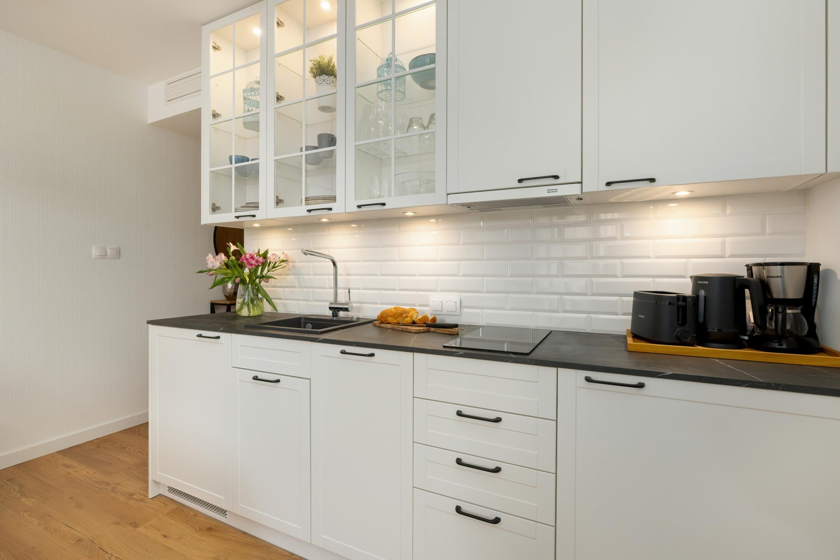 Una cocina moderna con armarios blancos, encimera negra y estufa empotrada.
