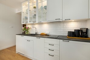A modern kitchen with white cabinetry, a black countertop, and a built-in stove. - Holiday Studio With Access to Pool and Sauna (Rewal)