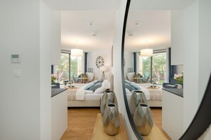 A modern bedroom with a large bed, bedside tables, a mirror, and a view of the outdoors. - Holiday Studio With Access to Pool and Sauna (Rewal)