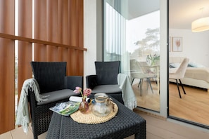 A modern room with two black wicker chairs, a small table with a woven placemat, a vase with flowers, and a glass jar. - Holiday Studio With Access to Pool and Sauna (Rewal)
