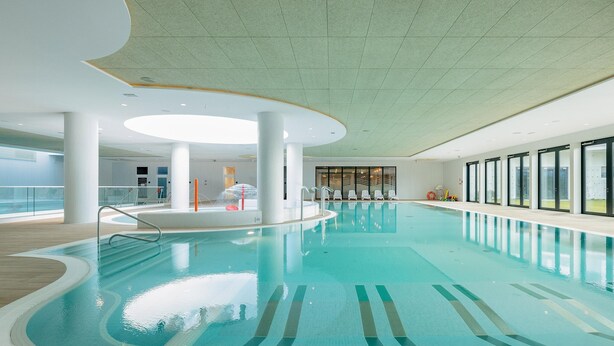 Una piscina interior amb marques clares de carrils, un disseny de sostre modern i grans finestres al costat.