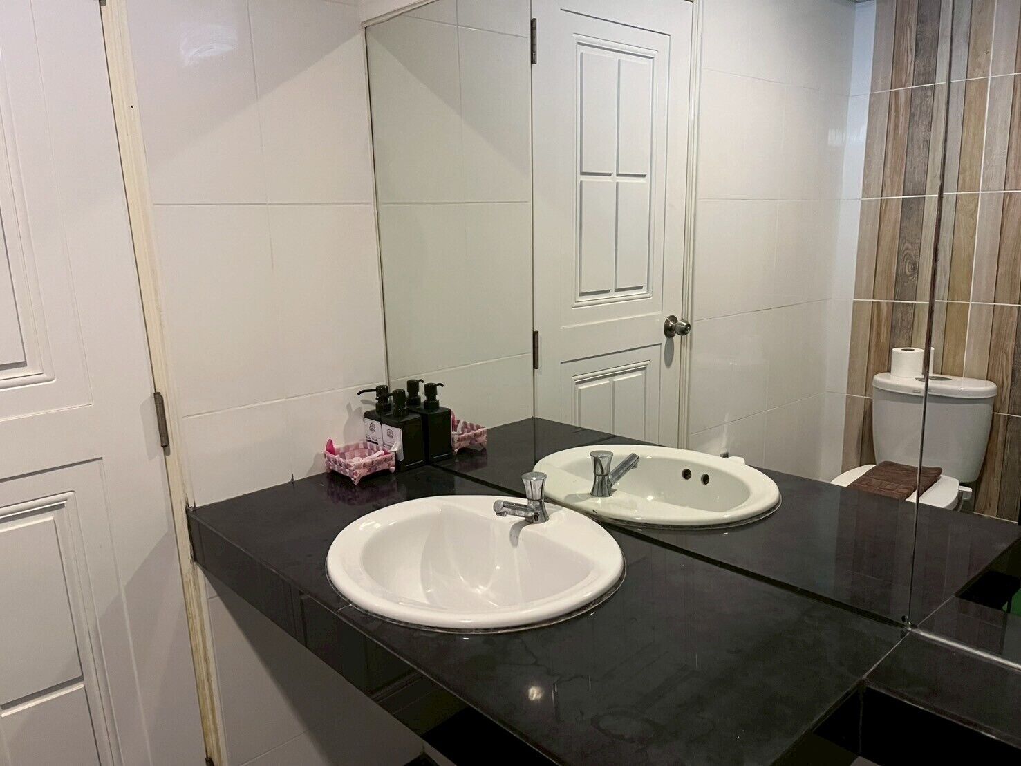 Et badeværelse med to håndvaske, et spejl, et toilet og en dør.