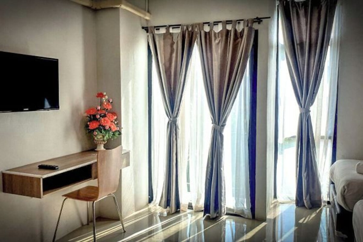 A modern room with a flat-screen TV mounted on the wall, a wooden desk with a chair, a vase with flowers, and a bed.
