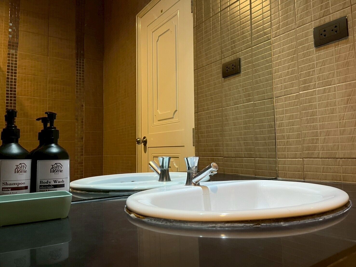 A bathroom with two sinks, a mirror, and two bottles of Toffy Home shampoo and body wash.