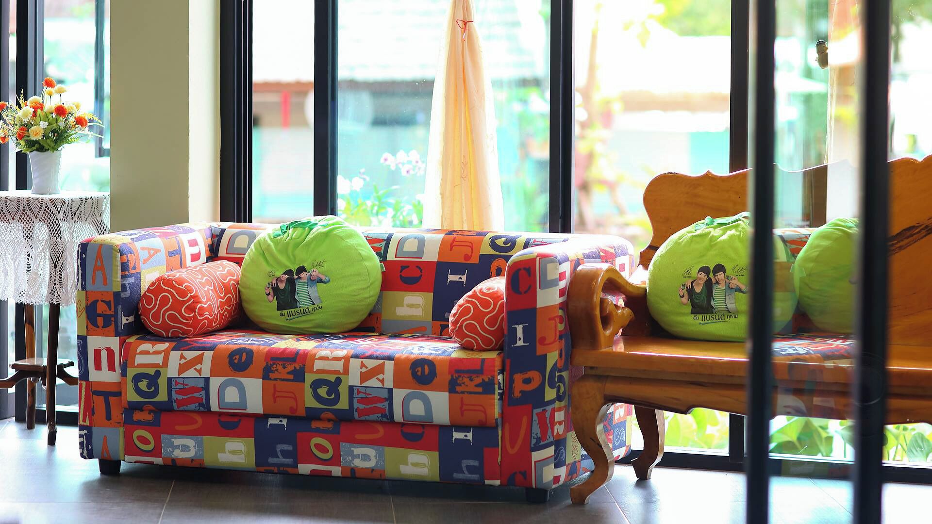 A colorful sofa with patterned cushions, a lace table, and a view through large windows.