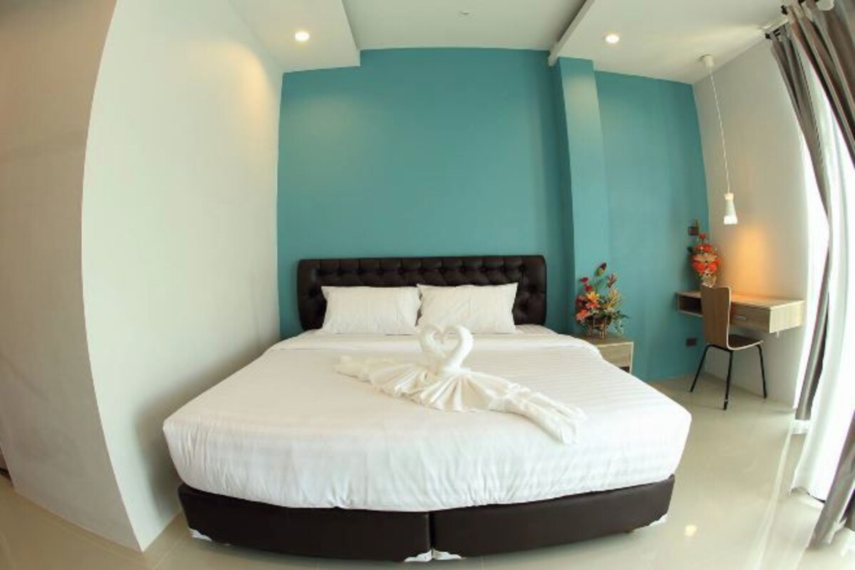 A hotel room with a large bed, a dark headboard, and a desk with a chair.