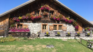 Un chalet traditionnel en bois, avec des murs en pierre, des volets en bois et des jardinières fleuries.