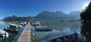 Un puerto deportivo con barcos amarrados, un muelle de madera y montañas al fondo.