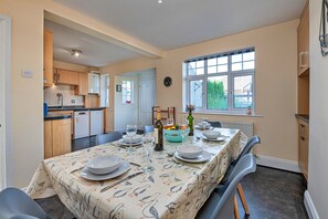 Un coin repas avec une table dressée pour quatre personnes, une cuisine en arrière-plan et une fenêtre donnant sur un paysage verdoyant.