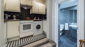 A compact kitchen with white cabinets, a black and white checkered floor, a washing machine, and a small oven. - Beautiful Apartment ac up to Six,12 min by Tube From Oxford Street,ac (London)