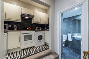 A compact kitchen with white cabinets, a black and white checkered floor, a washing machine, and a small oven. - Beautiful Apartment ac up to Six,12 min by Tube From Oxford Street,ac (London)