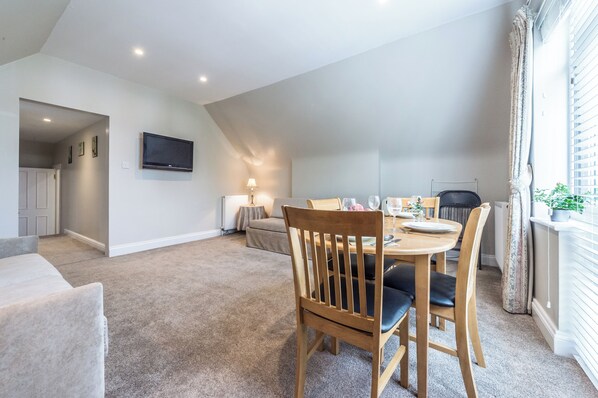 Un coin repas avec une table dressée pour quatre personnes, un canapé, un téléviseur fixé au mur et une fenêtre avec des rideaux.