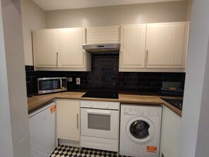 A compact kitchen with white cabinets, a microwave, an oven, and a washing machine. - Beautiful Apartment ac up to Six,12 min by Tube From Oxford Street,ac (London)