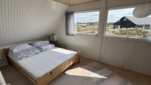 Un dormitorio con cama de madera, ventana con vistas a casas y vegetación, y un radiador en la pared.