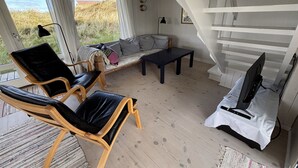 Un interior moderno con un sofá, dos sillones, una mesita, un televisor y una escalera.