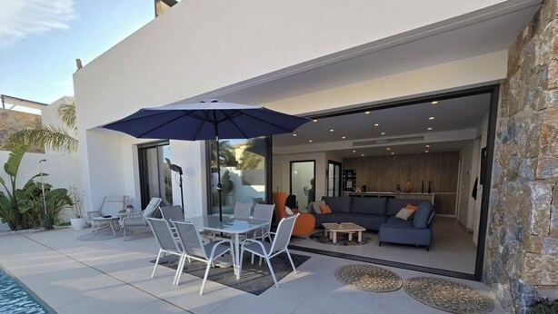 A modern outdoor patio with a pool, a dining area with a table and chairs, and a living room with a sofa and coffee table.