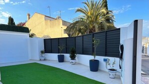 A rooftop garden with artificial grass, potted plants, and a modern fence.